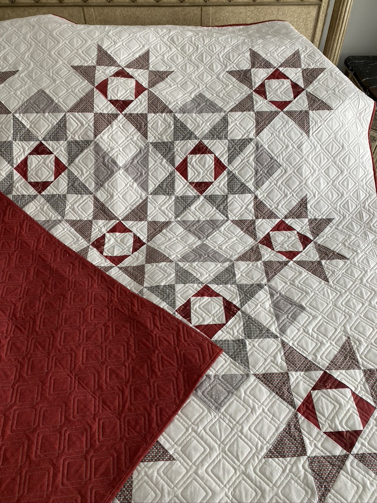 My first traditional quilt in cream, gray and red, with pieced star blocks and detailed quilting.